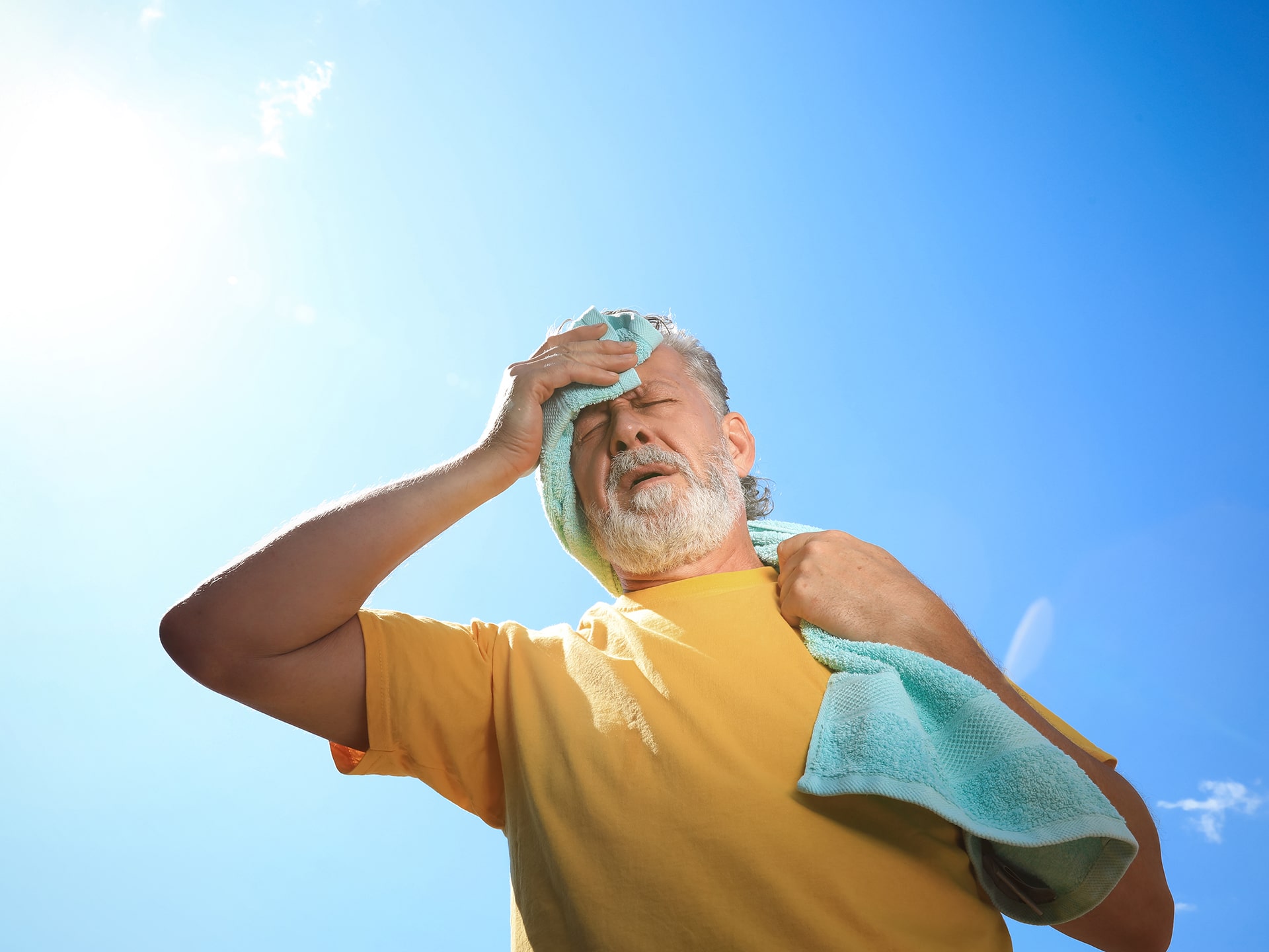 Senior man with towel suffering from heat stroke outdoors, low angle view